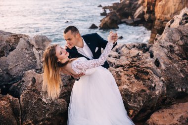 newlyweds are dancing among the rocks overlooking the ocean. the