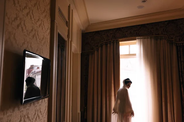 Невеста в халате у окна. уютная спальня с телевизором и — стоковое фото
