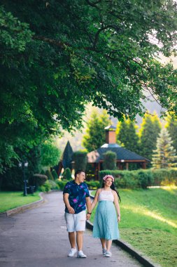 Young expectant mother and her husband hold hands and walking in