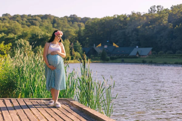 Jonge zwangere vrouw op een houten pier kijkt naar het meer. vrouw h — Stockfoto