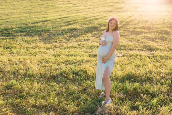 Jong zwanger vrouw in stijlvolle jurk en krans op haar hoofd op een — Stockfoto