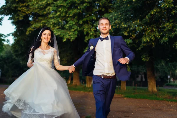 Newlyweds hold hands looking into the camera and running. bride — Stok fotoğraf