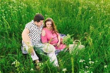 Müstakbel ebeveynler uzun otların arasında yorganın üzerinde oturuyorlar. çanta zekası