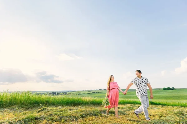 Pregnant woman in a pink dress holds a bouquet of flowers and ho — Stok fotoğraf