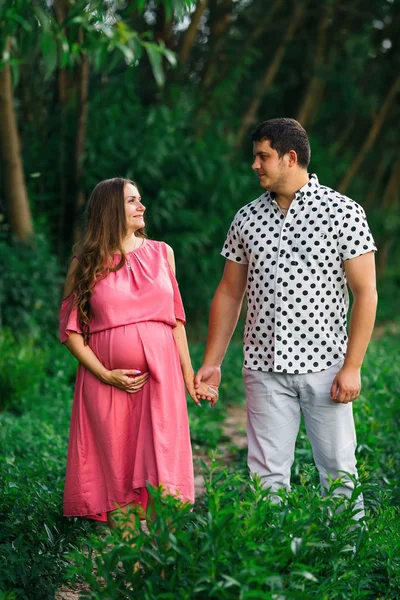Donna incinta in un abito rosa tocca delicatamente la pancia e un ma — Foto Stock