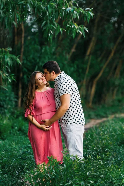 Pregnant woman in a pink dress gently touches her tummy and a ma — Stok fotoğraf