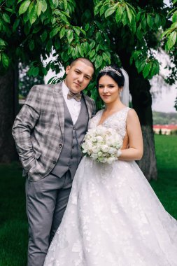 Gelin ve damat parktaki kameraya bakıyor. Gelin elinde beyaz w