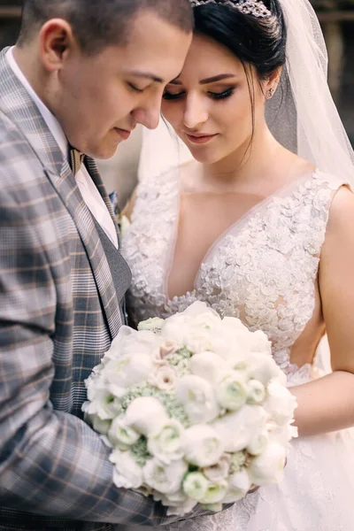 Braut und Bräutigam umarmen sich und betrachten einen schicken Hochzeitsstrauß. — Stockfoto