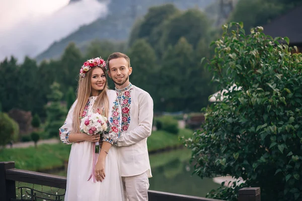 Recém-casados em roupas bordadas sorrindo e olhando para o veio — Fotografia de Stock