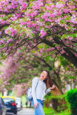 Gözlüklü kız ve kaldırımda bir sırt çantası Japon kiraz ağacının yanında.