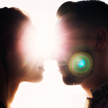 Yeni evliler yüz yüze duruyorlar ve yüzlerinin üst yarısı güneş ışınlarını kapatıyor.