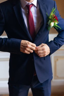 Şık mavi takım elbiseli ve kırmızı kravatlı damat ceketini iliklemiş. Güzel yaka çiçeği.
