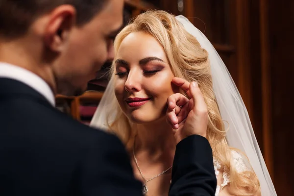 the bride with beautiful makeup closed her eyes and the groom touches her face with his hand.