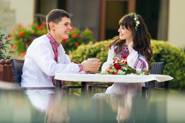 Novomanželé Vyšívaných Šatech Kavárně Popíjejí Horkou Kávu Usmívají Svatební Kytice — Stock fotografie