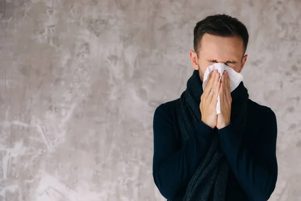 Sick man wearing scarf, blowing nose and sneeze into tissue. Male have flu, virus or allergy respiratory. Healthy, medicine and people concept. Headache and fever remedies.