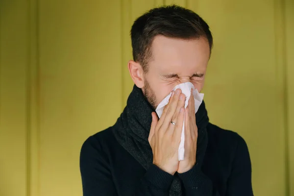 Sick man wearing scarf, blowing nose and sneeze into tissue. Male have flu, virus or allergy respiratory. Healthy, medicine and people concept. Headache and fever remedies.
