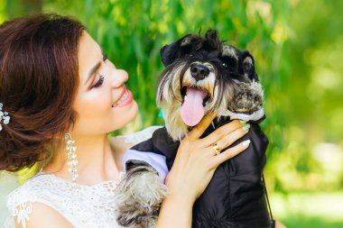 Gelin, pofuduk bir köpek schnauzer 'ını sigara içerken tutuyor. Güzel gelin gülümser ve kameraya bakar.