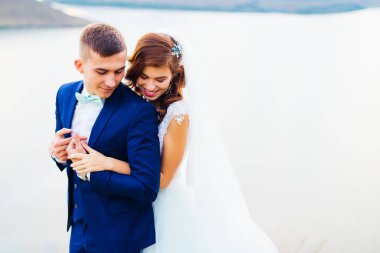 Gelin damadı arkadan kucaklıyor ve gülümsüyor. Akşam ve nehir