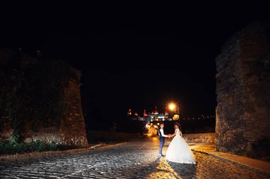 Damat gelini elle tutuyor. Işıklı ortaçağ kalesi. Gece yürüyüşü