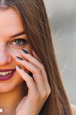 Yüzünün yarısı parlak makyajlı ve çilli bir kız. Kız kameraya bakar ve gülümser..