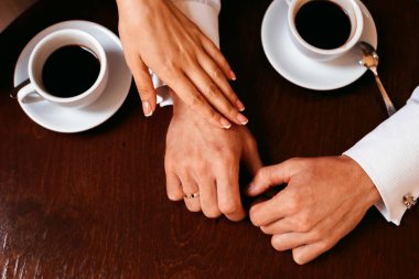 Gelin elini masaya koydu ve gelin de elini onun üzerine koydu. Sıcak kahve. en üstteki görünüm.