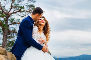 Damadın yakın çekimi gelini arkadan kucaklıyor ve birbirlerine bakıyorlar.