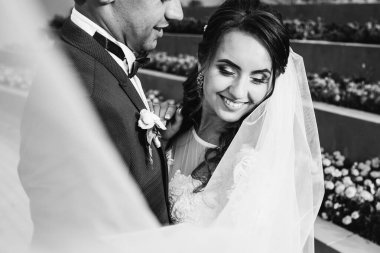 Damat, siyah beyaz fotoğrafçılığa gülümseyen ve gözlerini kapatan gelinini kucaklıyor.