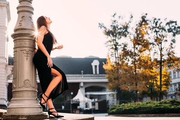 Sütunun yanındaki siyah elbiseli kızın profili. yapı ve sonbahar ağaçları.