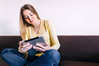 Kanepede dijital tablet kullanan çekici bir kadın.