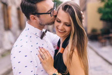 Adam kızı öpüyor. Kız gülümsüyor ve gözlerini kapıyor. Şehir sokağındaki çifte yakın çekim.