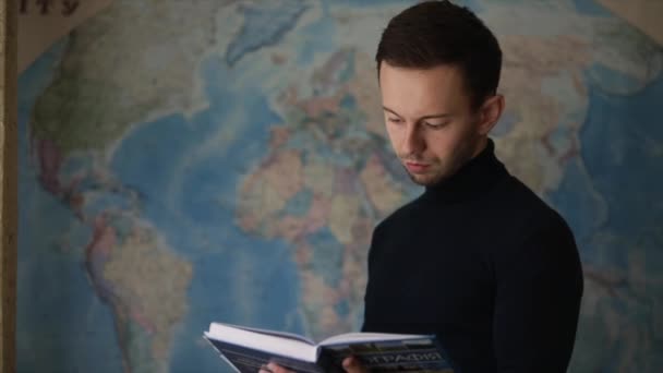 地理地図の近くで髭を生やした男が本を読む 学校に戻って 教室での授業 地理を簡単に学び — ストック動画