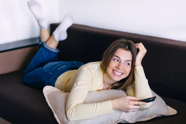 Νεαρή Χαμογελαστή Γυναίκα Βλέποντας Τηλεόραση Ενώ Βρίσκεται Στον Καναπέ Στο — Φωτογραφία Αρχείου