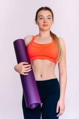 Beyaz arka planda menekşe yoga minderi tutan güzel kız. Moda, spor ve sağlıklı yaşam tarzı konsepti.