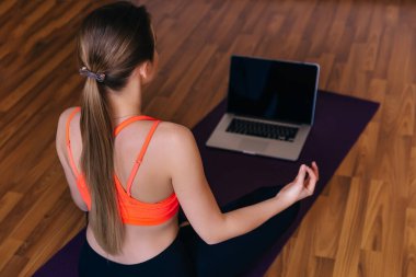 Turp gibi sağlam, sağlıklı, sakin bir kadın Lotus pozu verip internetten yoga dersi izliyor.