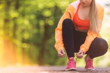 Dişi koşucu ayakkabılarını bağlıyor. Dışarıda koşuya hazırlanıyor.