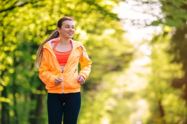 Genç bir kadın spor kıyafetleri içinde parkta koşuyor.