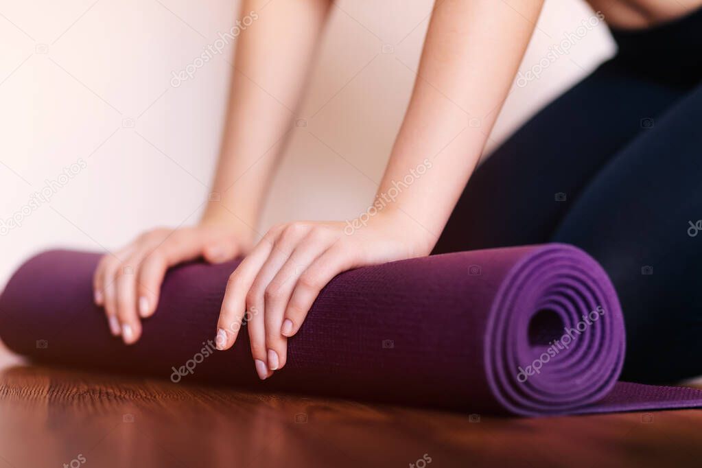 Close-up of woman folding violet yoga or fitness mat after workout at home in the living room. Healthy lifestyle, keep fit concept.