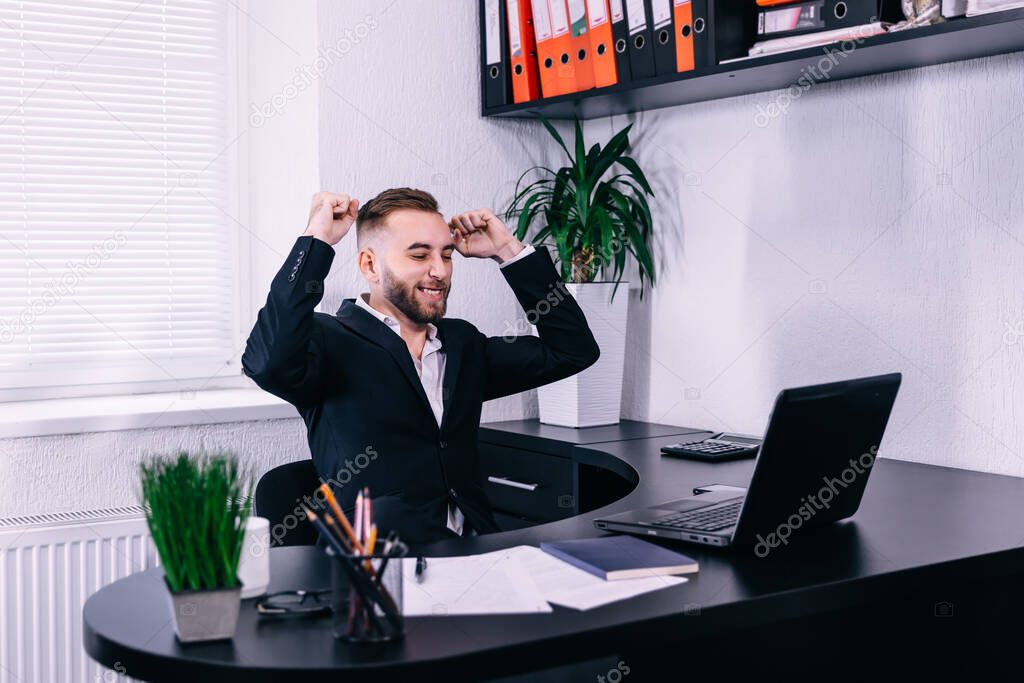 Photo of happy businessman in office near computer make winner gesture.