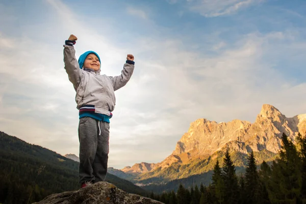 A child conquers the summit, loose his proud arms, in the backgr — Stock Photo, Image