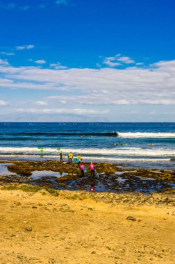 Gün doğumunda bir grup kız ve erkek Playa de Las Americas 'ta sörf kursuna başlamak için okyanusa giriyor. 11 Nisan 2019. Santa Cruz de Tenerife İspanya Afrika. Seyahat Turizmi Sokak Fotoğrafçılığı.