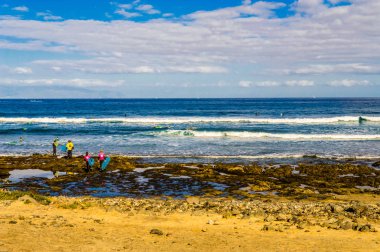 Gün doğumunda bir grup kız ve erkek Playa de Las Americas 'ta sörf kursuna başlamak için okyanusa giriyor. 11 Nisan 2019. Santa Cruz de Tenerife İspanya Afrika. Seyahat Turizmi Sokak Fotoğrafçılığı.