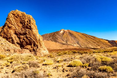 El Teide Ulusal Parkı 'nda güneşli ve çok açık bir günde büyük bir lav kayasının arkasındaki en yüksek tepe. 13 Nisan 2019. Santa Cruz de Tenerife İspanya Afrika. Seyahat Turizmi Sokak Fotoğrafçılığı.