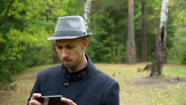 En man i hatt och rock i regnet tittar på något i telefonen — Stockvideo