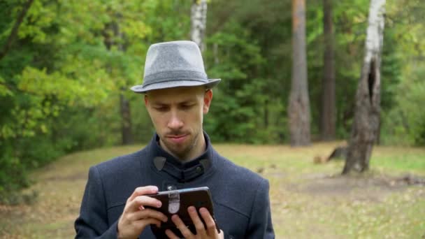 Un homme en chapeau et manteau sous la pluie regardant quelque chose au téléphone — Video