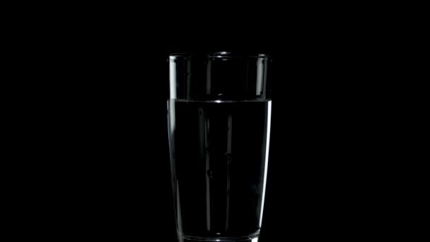 Een glas water draait in het donker — Stockvideo