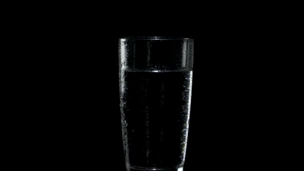 Un verre d'eau avec des gouttes à l'extérieur tourne dans l'obscurité 