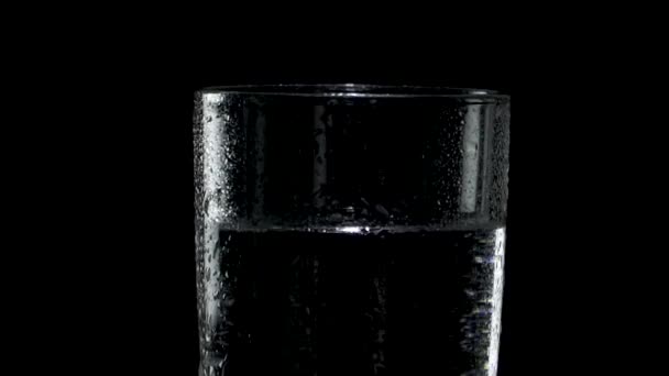 Ein nasses Glas Wasser dreht sich im Dunkeln und entfernt sich — Stockvideo