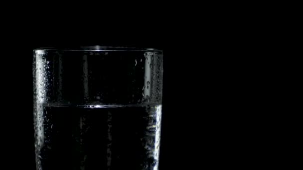 Close-up van een nat glas water dat links in het donker draait — Stockvideo