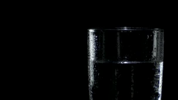 Zbliżenie mokrej szklanki wody, która obraca się w ciemności po prawej stronie — Wideo stockowe