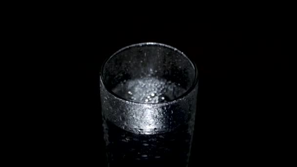 Un vaso húmedo de agua gira en la oscuridad, brillando con luz — Vídeos de Stock